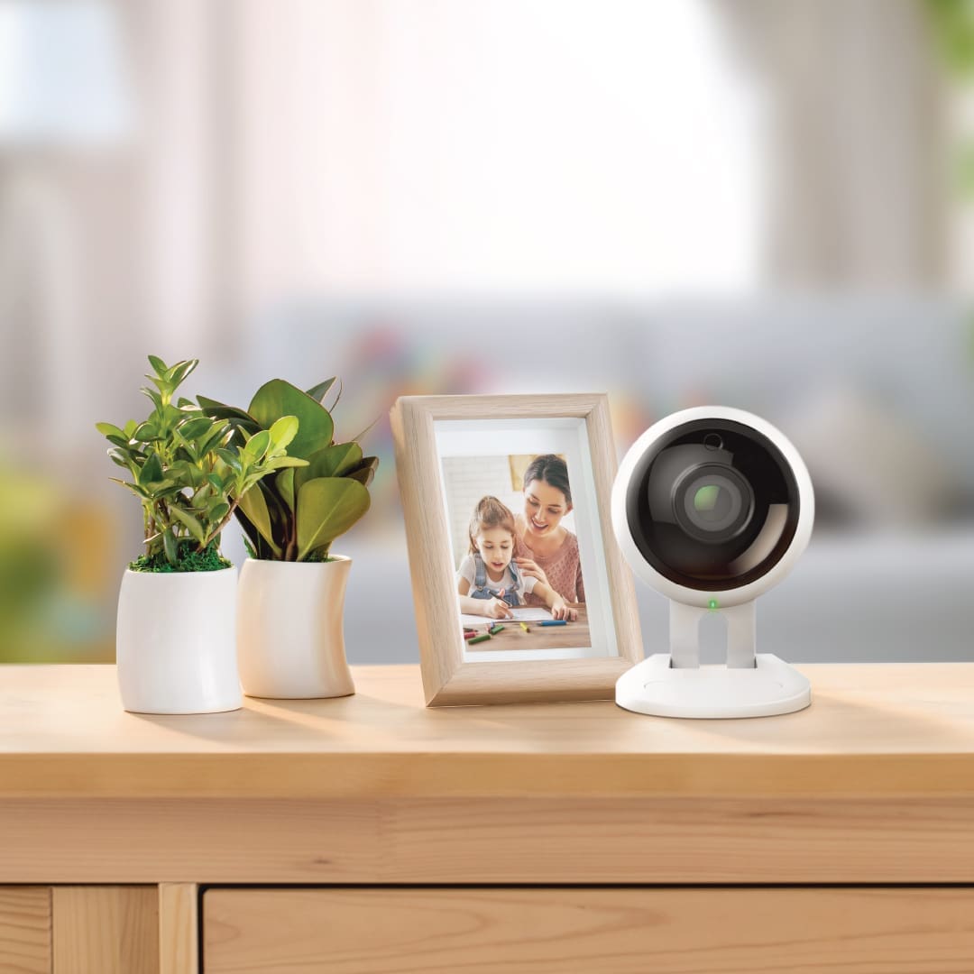 A Samsung 'BabyView' camera on a wooden sideboard with a framed photo and potted plants