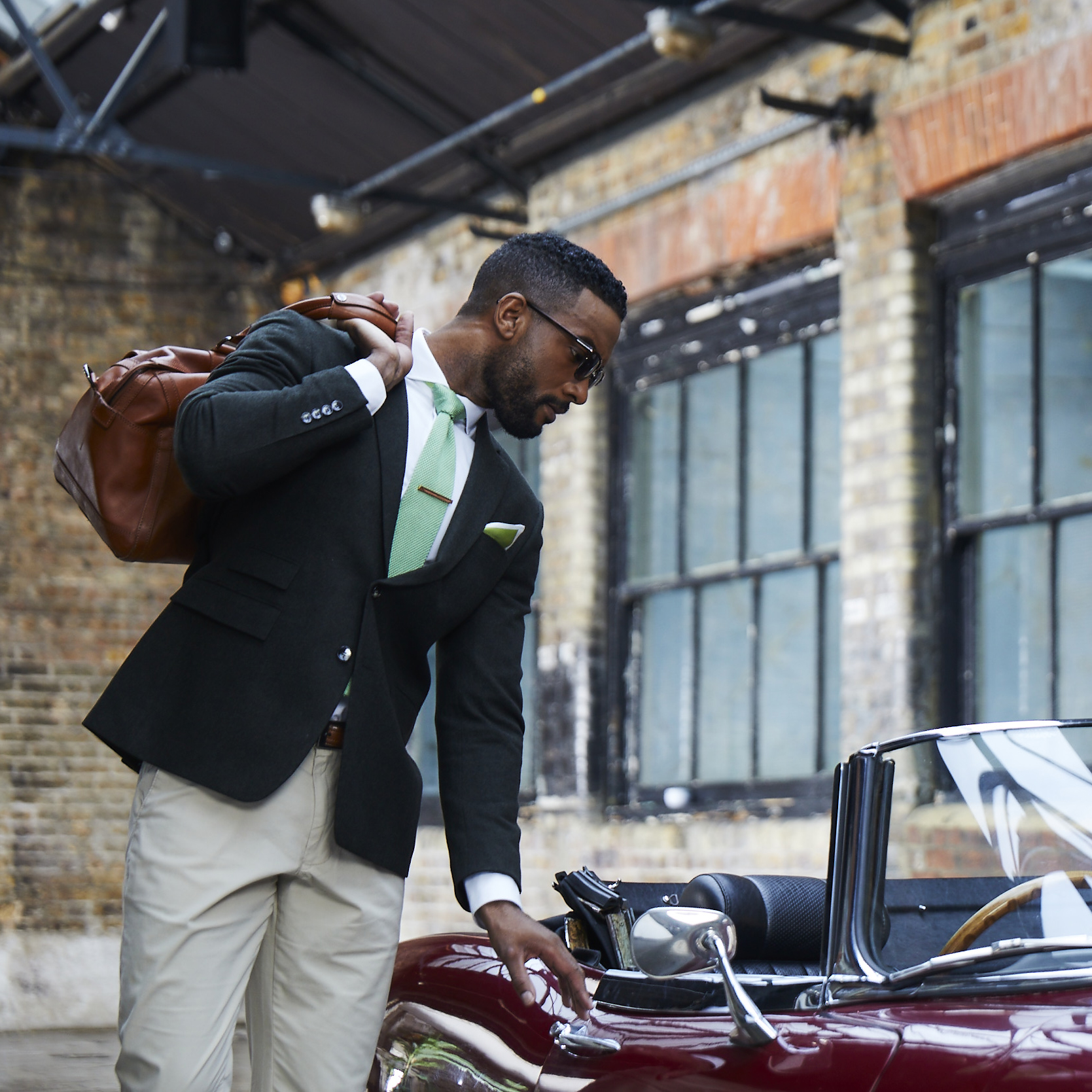Stylish black man in suit with leather bag getting into a red convertible classic car